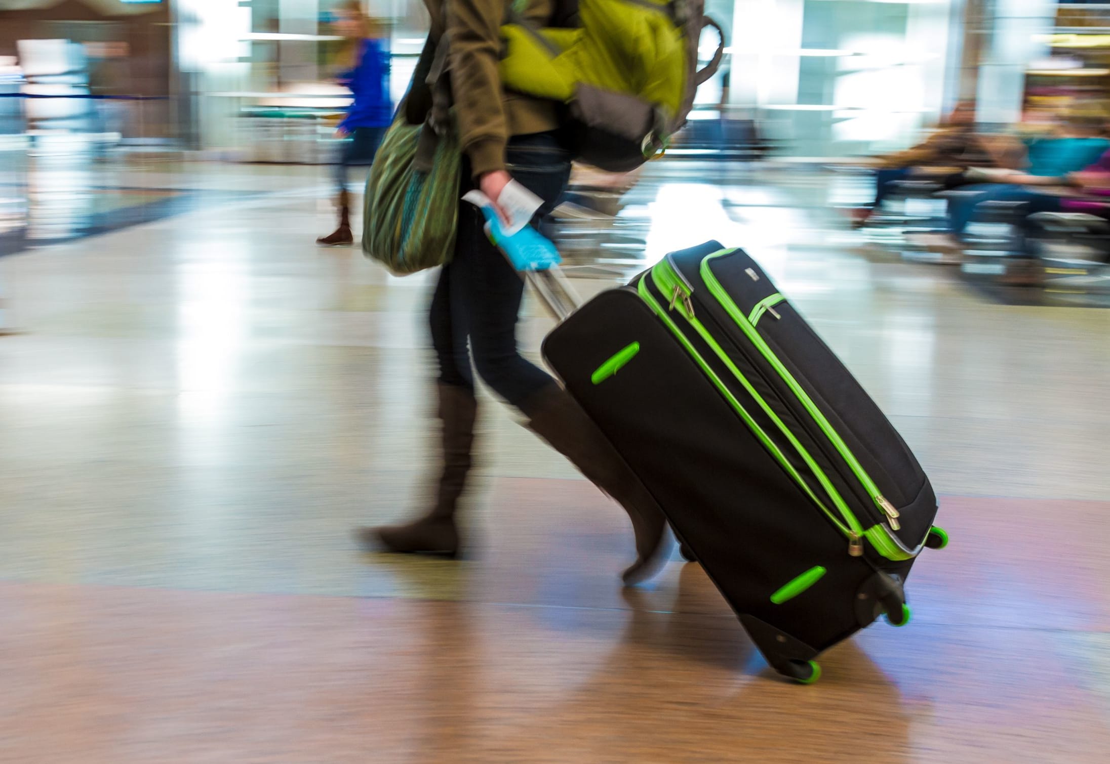 A woman with a backpack pulls a suitcase through an airport.