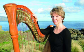NZSO harpist Carolyn Mills stands beside her harp, with Wellington's south coast in the background.