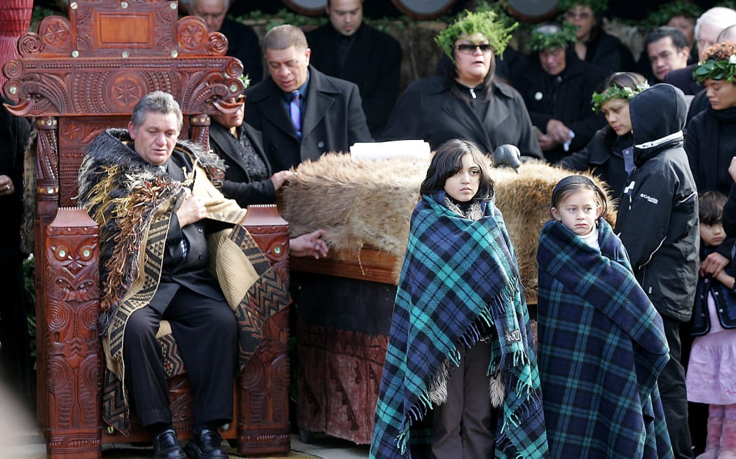 New Maori King Tuheitia Paki (L) sits on the carved wooden throne alongside the feather-cloak draped coffin of his mother Te Arikinui Dame Te Atairangikaahu during the funeral service at Turangawaewae in Ngaruawahia, south of Auckland, 21 August 2006.  New Zealand's indigenous Maori announced a new monarch 21 August during the funeral of Te Arikinui Dame Te Atairangikaahu, who died last week after a 40-year reign.    AFP PHOTO/Peter Drury/POOL (Photo by PETER DRURY / POOL / AFP)