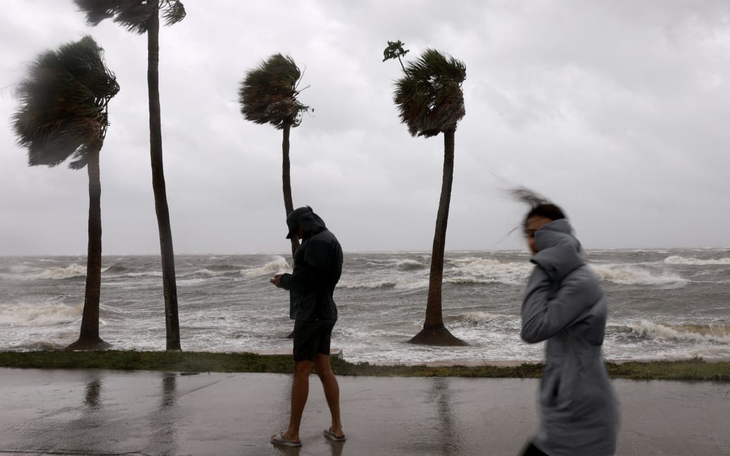 People walk in the wind and rain next to Tampa Bay as Hurricane Helene churns offshore on 26 September, 2024, at St. Petersburg, Florida.