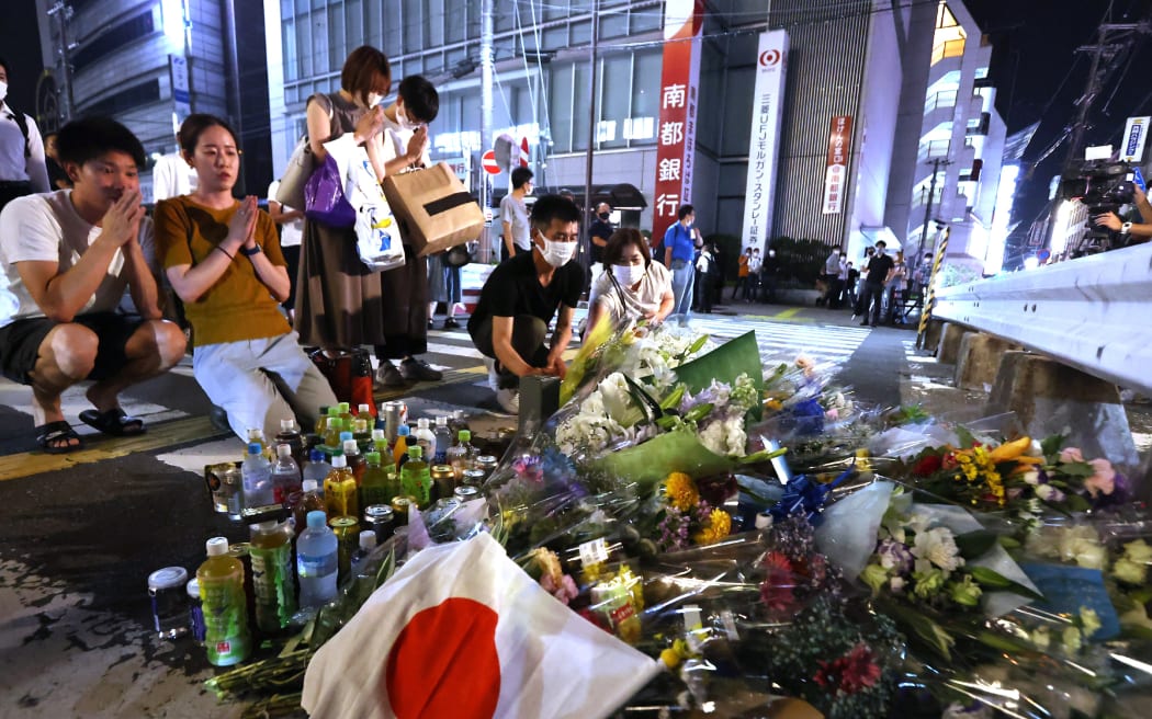 People lay a bouquet of flowers and offer a plastic bottle with a Japanese national flag at the site where former Prime Minister Shinzo Abe was shot to death near Yamato Saidaiji Station in Nara Prefecture on July 8, 2022. Abe went on a stumping tour for supporting his party member candidate in the House of Councillors election.  67-year-old Abe has been shot in the chest and has been confirmed dead at Nara Medical University Hospital. ( The Yomiuri Shimbun ) (Photo by Osamu Kanazawa / Yomiuri / The Yomiuri Shimbun via AFP)
