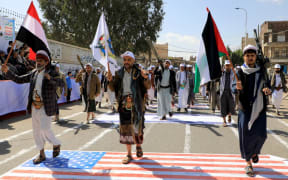 Armed Yemeni men step over a US and an Israeli flag painted on the asphalt in the Houthi-run capital Sanaa, during a march in support of the Palestinians amid ongoing battles between Israel and Hamas militants in the Gaza Strip, on February 29, 2024. (Photo by MOHAMMED HUWAIS / AFP)