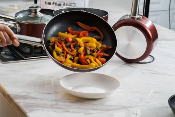 A non-stick pan with food being tipped to empty stir fry food into plate.
