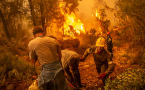 Firefighter and volunteers use a water hose near a burning blaze trying to extinguish a fire in the village of Glatsona on Evia island.