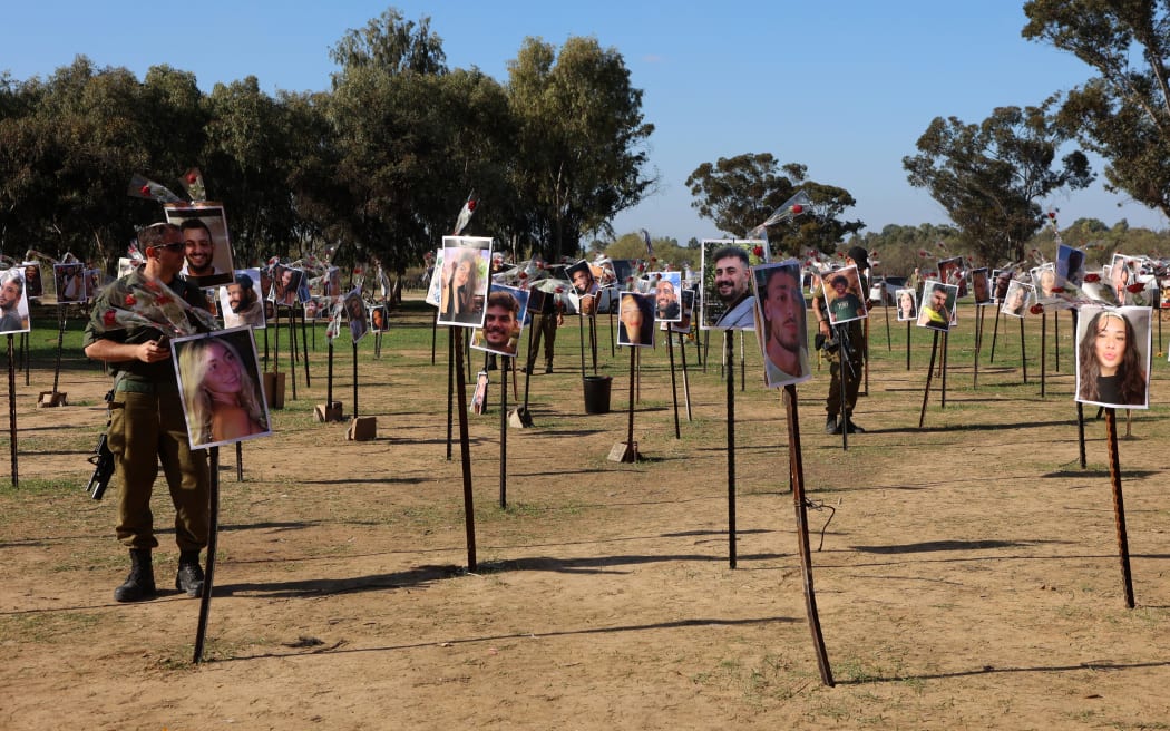 Israeli soldiers walk on 30 November 2023 among the pictures of people taken captive or killed by Hamas militants duing the Supernova music festival on 7 October, at the site where the deadly incident took place near Kibbutz Reim in southern Israel.