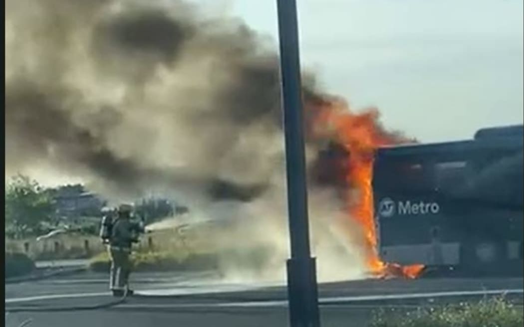 A firefighter uses a water hose to douse flames on an Auckland Transport Metro bus.
