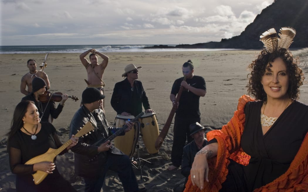 Moana and The Tribe with instruments, on a beach.