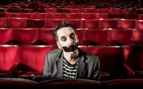 TapeFace sitting in a theatre in costume with tape over his mouth