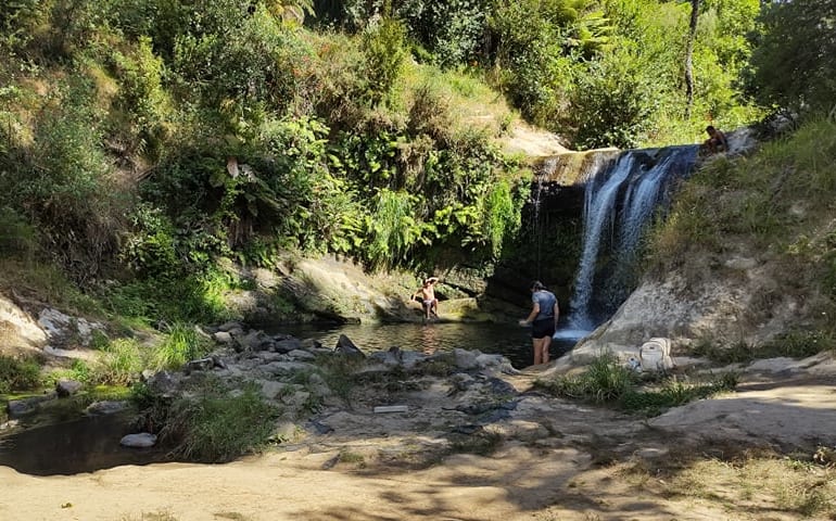 A waterfall with swimmers at the bottom.