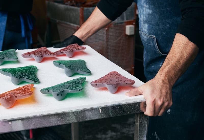 A pair of gloved hands holding a tray of coloured glass airplane sculptures.