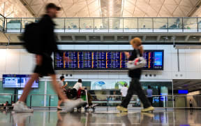 Passengers walk past a flight information board at the Hong Kong International Airport.