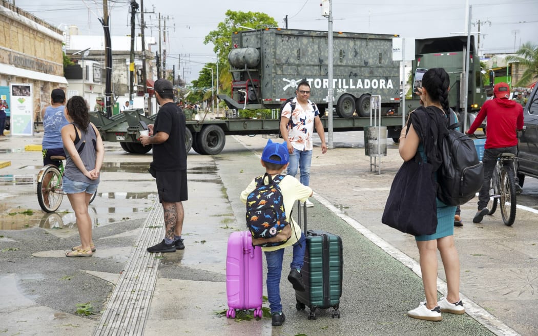 Tourists stand on a street as Mexican army soldiers, members of the DN-III (Natural Disasters) plan, arrive with a mobile kitchen team to assist the population affected by the passage of Hurricane Beryl in Tulum, Quintana Roo State, Mexico, on July 5, 2024. Hurricane Beryl slammed into Mexico's Yucatan Peninsula Friday near the resort town of Tulum with fierce winds, US forecasters said. The National Hurricane Center said the storm was packing maximum sustained winds of 100 mph (160 kph) making it a Category 2 hurricane, weaker than earlier in the week as Beryl hit islands in the Caribbean. (Photo by Elizabeth RUIZ / AFP)