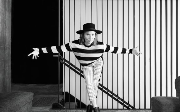 A black and white photo of singer songwriter KT Tunstall wearing stripey clothing, bowing in front of a striped wall.
