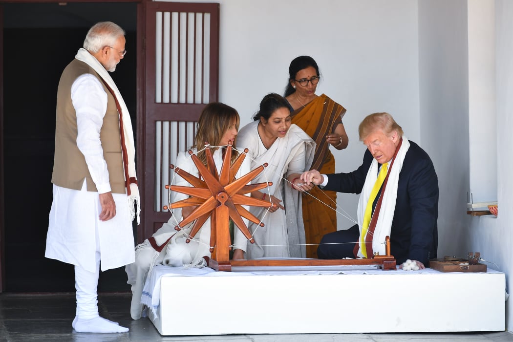 US President Donald Trump holds a string while checking a charkha, or spinning wheel, as First Lady Melania Trump and India's Prime Minister Narendra Modi look on during their visit at the Gandhi Ashram on 24 February, 2020.