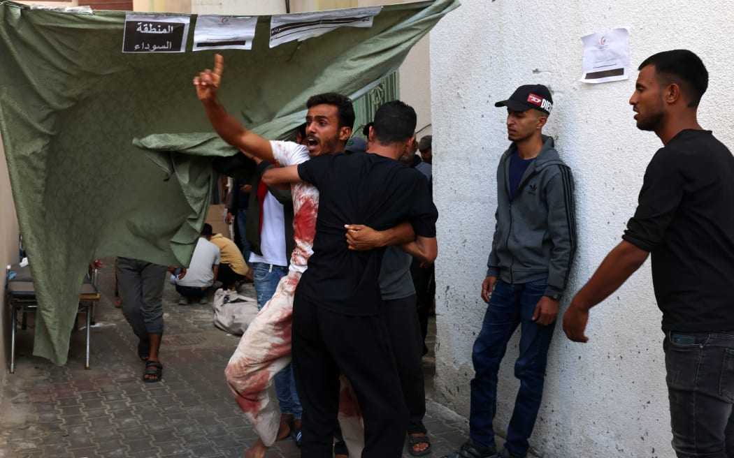 A blood-covered man reacts after recognising a person killed in an Israeli strike, outside a makeshift morgue marked "the black zone" in the yard of the Kuwait hospital, in Rafah in the southern Gaza Strip, on October 22, 2023.
