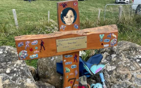 A memorial cross for O'siah Prasad covered in stickers, toys and flowers.