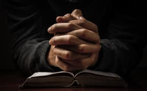 Hands of a man praying in solitude with his Bible.