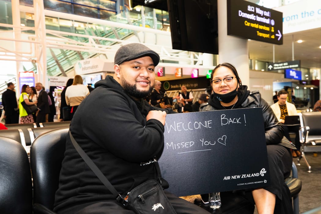 People waiting at Auckland Airport hold a 'welcome' sign as they wait for passengers to disembark from first flight from Sydney to Auckland under the trans-Tasman bubble arrangement.