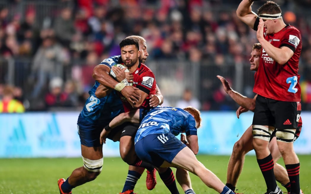 Richie Mo'unga of the Crusaders is tackled by Patrick Tuipulotu of the Blues and Finlay Christie of the Blues during the Super Rugby Aotearoa,
