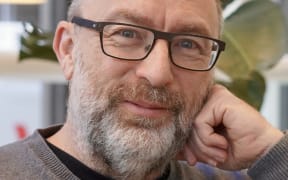 Jimmy Wales is a smiling bespectacled and bearded man in a grey sweater.