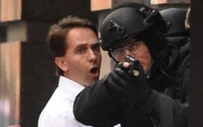 Two hostages run for cover behind a policeman.