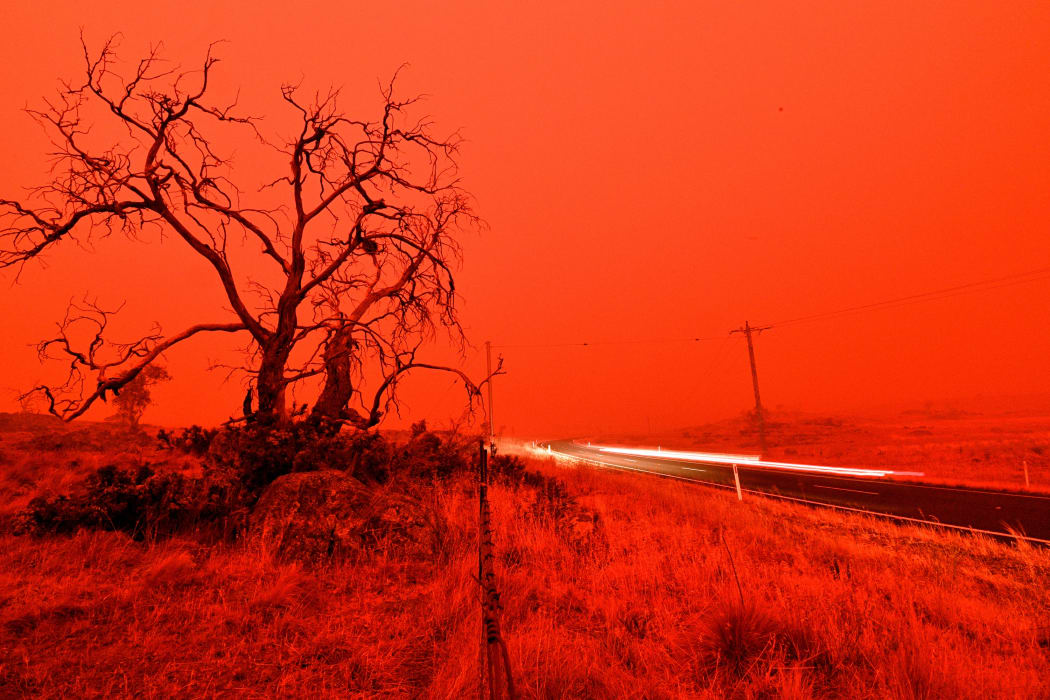 A long exposure picture shows a car commuting on a road as the sky turns red from smoke of the Snowy Valley bushfire on the outskirts of Cooma on January 4, 2020.