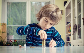 A photo of a little boy making stack of coins, counting money at table. Learning financial responsibility and planning savings concept.