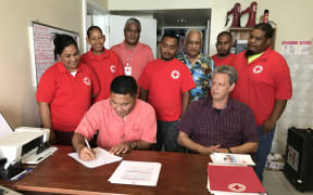 Marshall Islands Minister of Health Kalani Kaneko signs an agreement with the Marshall Islands Red Cross Society for cooperation in first aid training as Red Cross Secretary General Jack Niedenthal (sitting) and staff and volunteers look on.