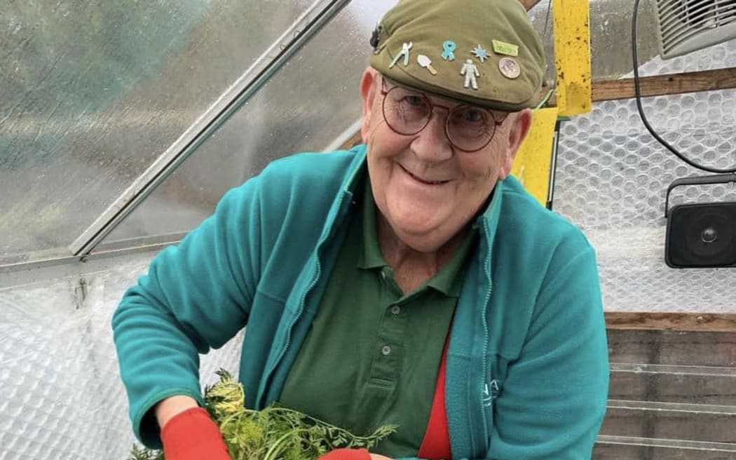Social media star and gardener Gerald Stratford smiles as he holds up a large bunch of carrots inside a green house
