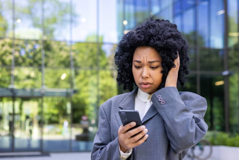 Young woman outside office news reading bad news online, businesswoman using app on smartphone while walking in city, female worker holding phone, sad and disappointed.