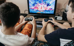 Two Boys playing Fortnite online video game. Two teenager holding Joystick in front of the monitor screen with logo of game Fortnite from Epic Games. Kropivnitskiy, Ukraine, July 01, 2020