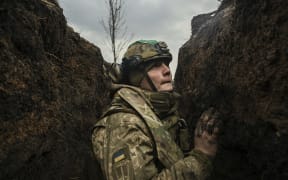 A Ukrainian serviceman takes cover in a trench during shelling next to a 105mm howitzer  near the city of Bakhmut, on March 8, 2023, amid the Russian invasion of Ukraine. (Photo by Aris Messinis / AFP)