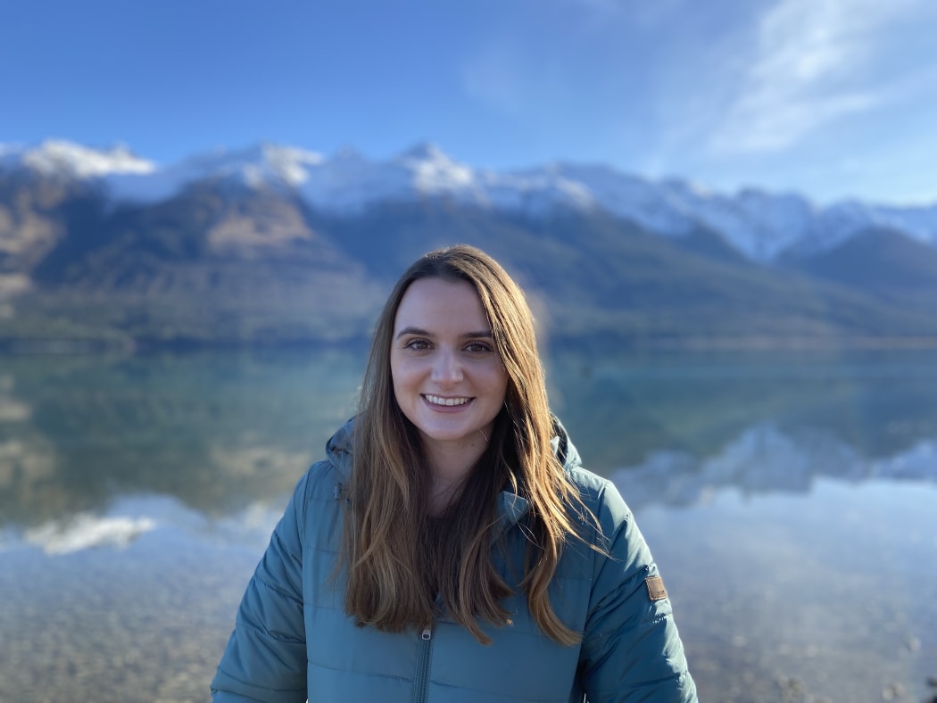 Anna Blair stands in front of Wakatipu lake on a sunny day