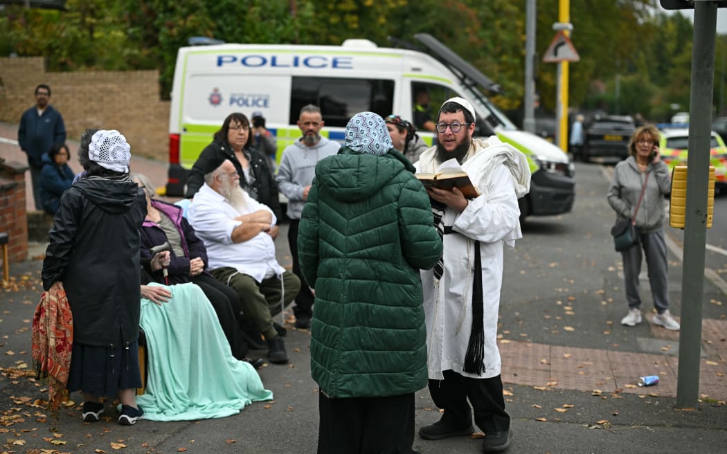 Members of the local Jewish community stand in the street outside Heaton Park Hebrew Congregation synagogue in Crumpsall, north Manchester, on October 2, 2025, following an attack at the synagogue. Two people were killed and three wounded in a car ramming and stabbing incident outside a synagogue in Manchester, northwest England, on Thursday, police said. "A man believed to be the offender was shot by GMP (Greater Manchester Police) Firearms Officers and is also believed to be deceased," the force said on X, adding his death could not yet be confirmed due to "suspicious items on his person". (Photo by Oli SCARFF / AFP)
