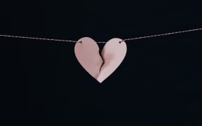 Stylised image of two halves of a pale pink broken heart threaded on string against a black background.