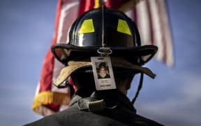 A firefighter wearing the photo badge of a victim on his helmet, pauses for a moment of silence on September 11, 2021 in  Morrison, outside Denver, Colorado.