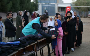 A worker of the Cansuyu Charity and Solidarity Organization gives a school bag to an Afghan child as the organisation distributes aid to orphans with the support of donators in Kabul, Afghanistan on 6 November, 2022.
