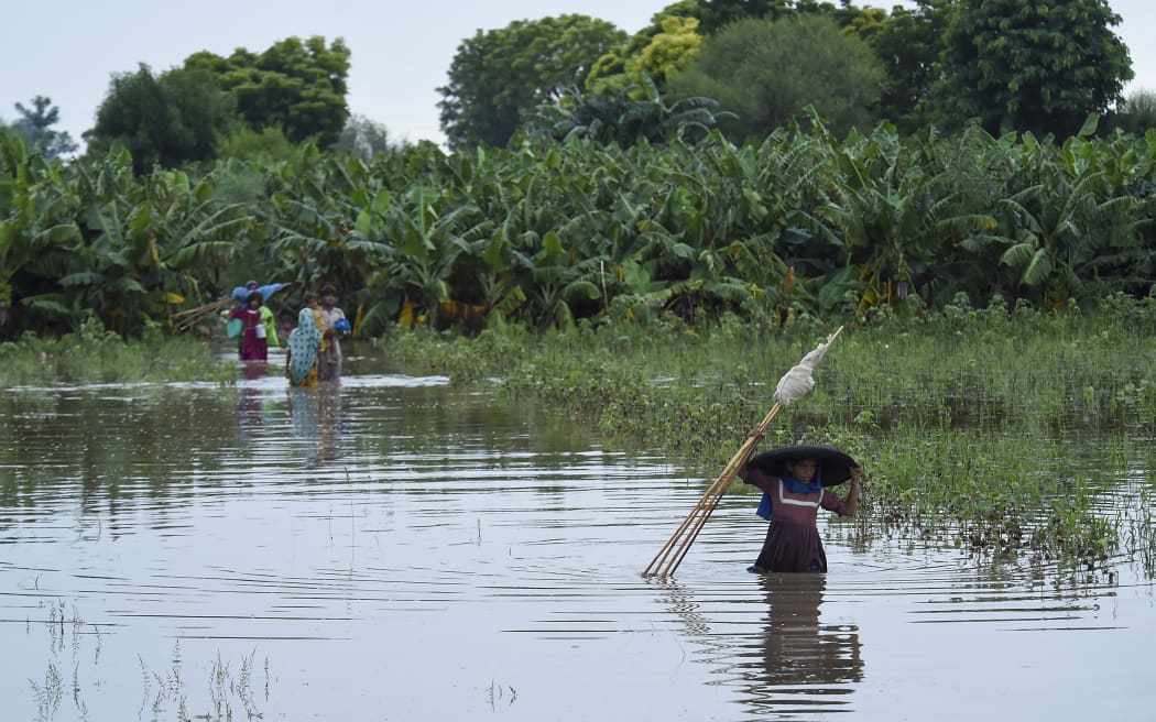 Stranded people wade through a flooded area after heavy monsoon rainfall in the Nawābshāh district of Sindh province, southern Pakistan on 25 August, 2022.