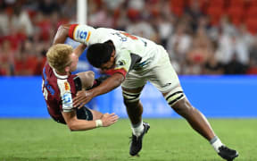 Tom Lynagh (left) of the Reds is tackled after passing the ball by Samipeni Finau of the Chiefs.