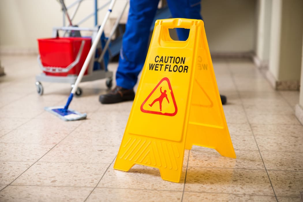 Worker Mopping Floor With Wet Floor Caution Sign On Floor