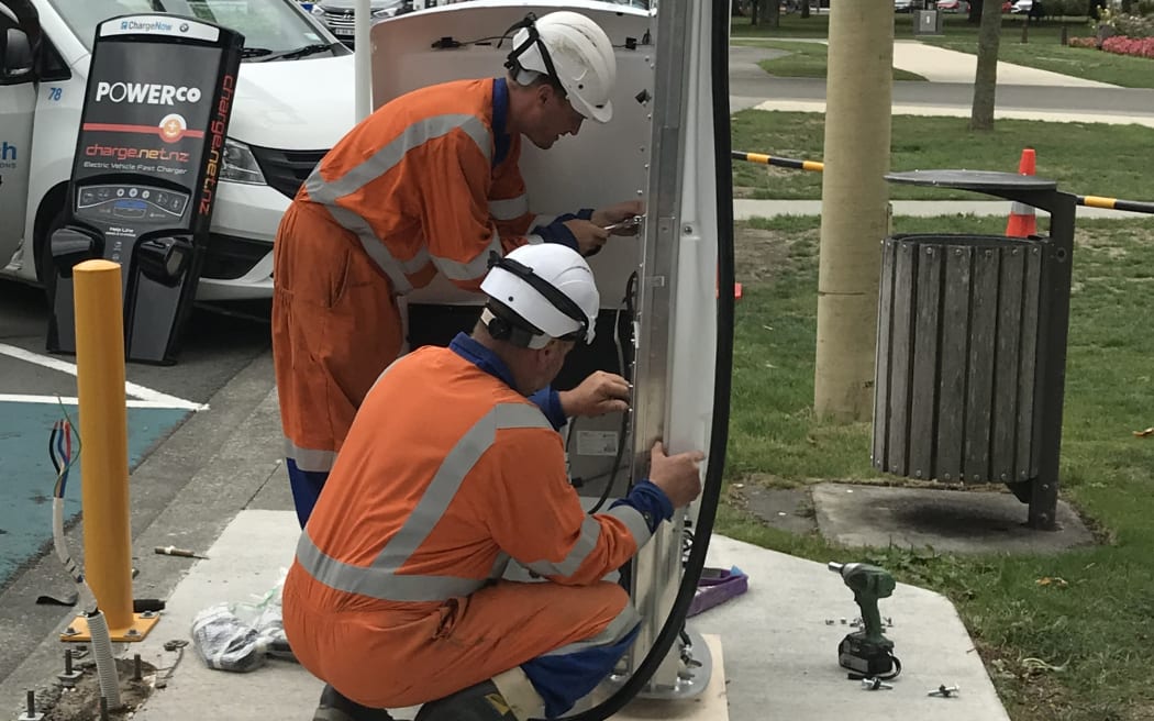 Two electricians work on an EV charging station.
