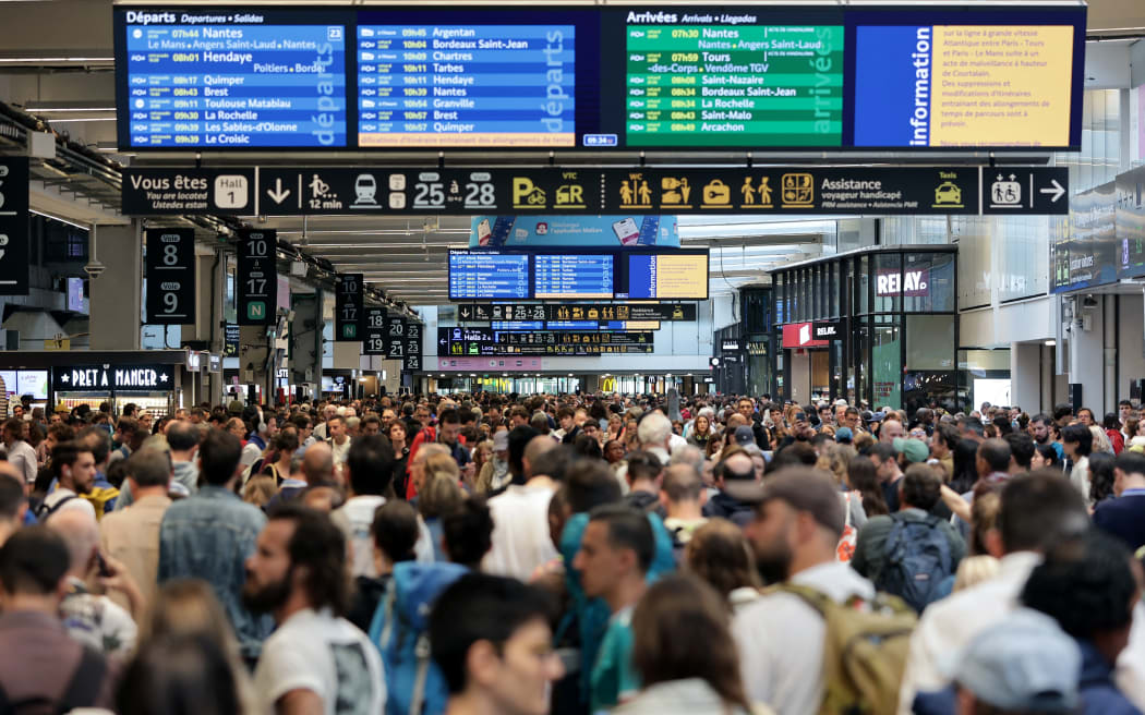 Passengers gather around the departure and arrival boards at the Gare Montparnasse train station in Paris on July 26, 2024 as France's high-speed rail network was hit by malicious acts disrupting the transport system hours before the opening ceremony of the Paris 2024 Olympic Games. According to SNCF a massive attack on a large scale hit the TGV network and many routes will have to be cancelled. SNCF urged passengers to postpone their trips and stay away from train stations. (Photo by Thibaud MORITZ / AFP)