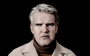 Lloyd Cole in a beige jacket looking into the distance.