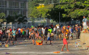 This screen grab from AFPTV video footage taken on January 10, 2024 shows people carrying items as crowds leave shops with looted goods amid a state of unrest in Port Moresby. A festering pay dispute involving Papua New Guinea's security forces on January 10 sparked angry protests in the capital, where a crowd torched a police car outside the prime minister's office. By Wednesday afternoon pockets of unrest had spread through the capital Port Moresby, with video clips on social media showing crowds looting shops and stretched police scrambling to restore order.