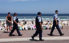 The Police walk past floral tributes left at the promenade of Bondi Beach in Sydney on 18 December, 2025, to honour victims of the shooting that took place there on 14 December.