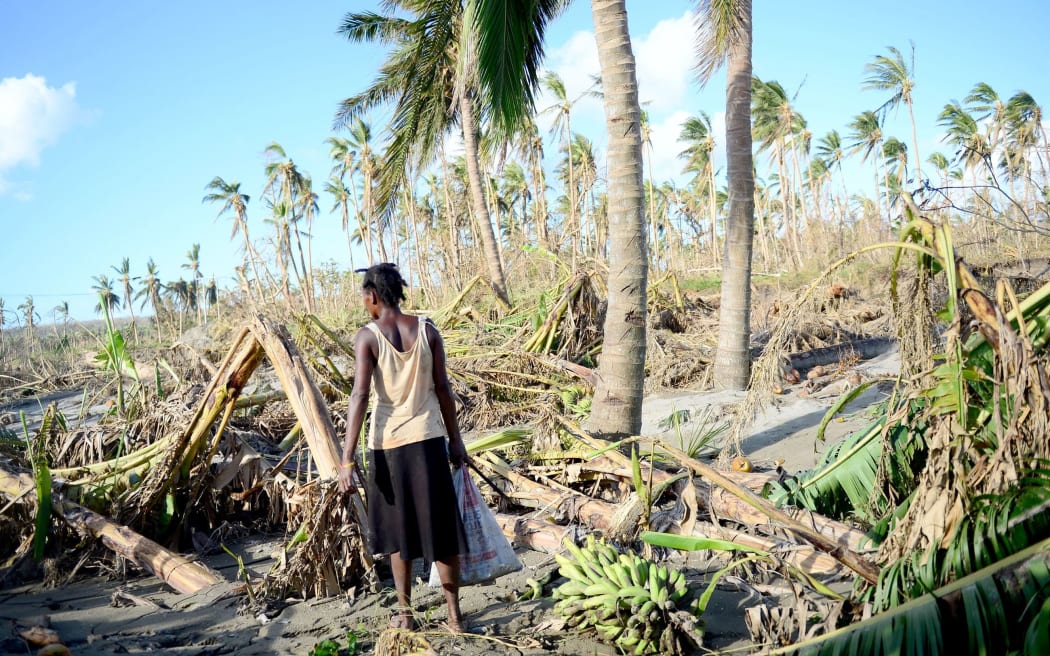 A woman carries bananas found amid the destruction caused by Cyclone Pam.