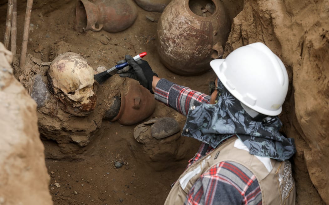 An archaeologist cleans a skull attributed to the pre-Inca Chancay culture accidentally unearthed by workers installing a gas pipeline in Lima's Puente Piedra district, on July 31, 2025. (Photo by CONNIE FRANCE / AFP)