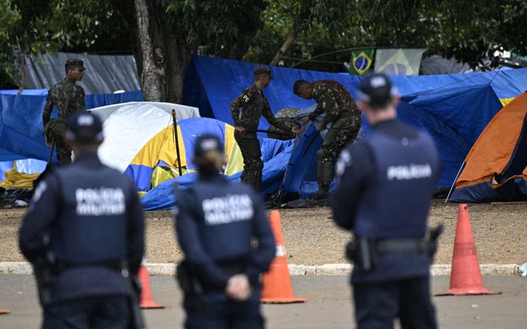 Soldiers dismantle a camp by supporters of Brazil's far-right ex-president Jair Bolsonaro that had been set up in front of the Army headquarters in Brasilia, on January 9, 2023, as police forces stand guard a day after backers of the ex-president invaded the Congress, presidential palace and Supreme Court. - Brazilian security forces locked down the area around Congress, the presidential palace and the Supreme Court Monday, a day after supporters of ex-president Jair Bolsonaro stormed the seat of power in riots that triggered an international outcry. Hardline Bolsonaro supporters have been protesting outside army bases calling for a military intervention to stop Lula from taking power since his election win. (Photo by Mauro PIMENTEL / AFP)