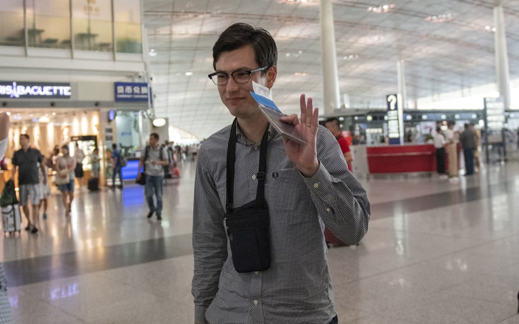 Alek Sigley, an Australian student who was detained in North Korea, waves while holding his passport and flight ticket as he walks for his departure at the Beijing International airport on July 4, 2019. )