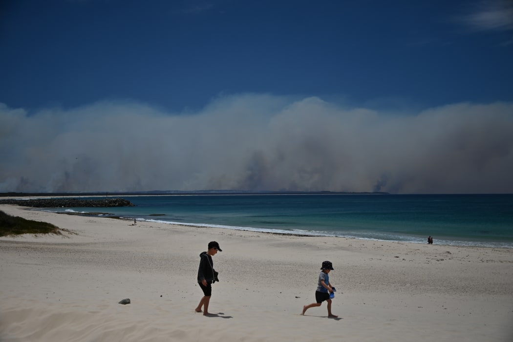 Bushfires burn in the distance as children play on a beach in Forster, 300km north of Sydney, on 9 November, 2019.